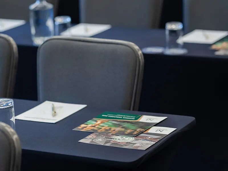 Sala de evento corporativo montada con mesas vestidas, libretas y servicio de bebidas
