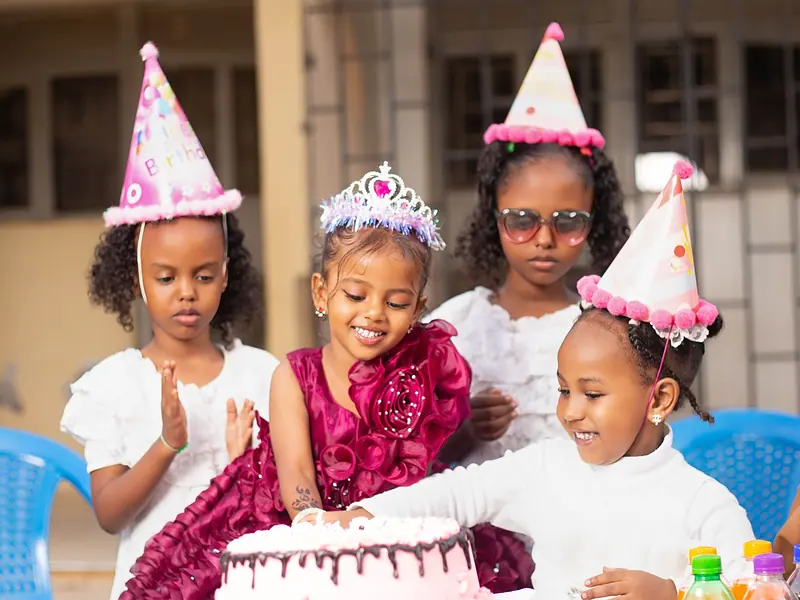 Niños con gorros de fiesta celebrando un cumpleaños infantil alrededor del pastel