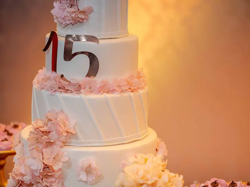 Pastel de XV años de tres pisos decorado con flores de azúcar en tonos rosa