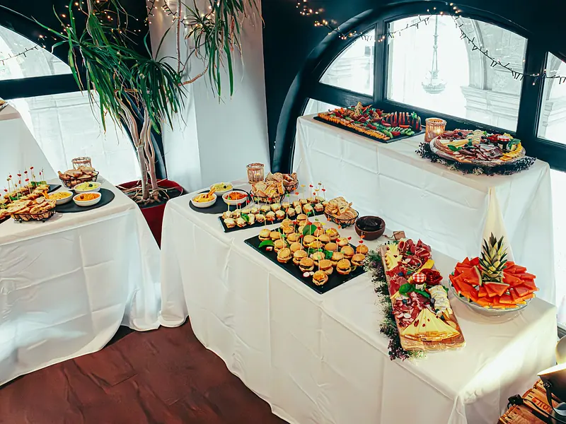 Montaje de catering para evento corporativo con bocadillos, canapés y fruta en mesas vestidas