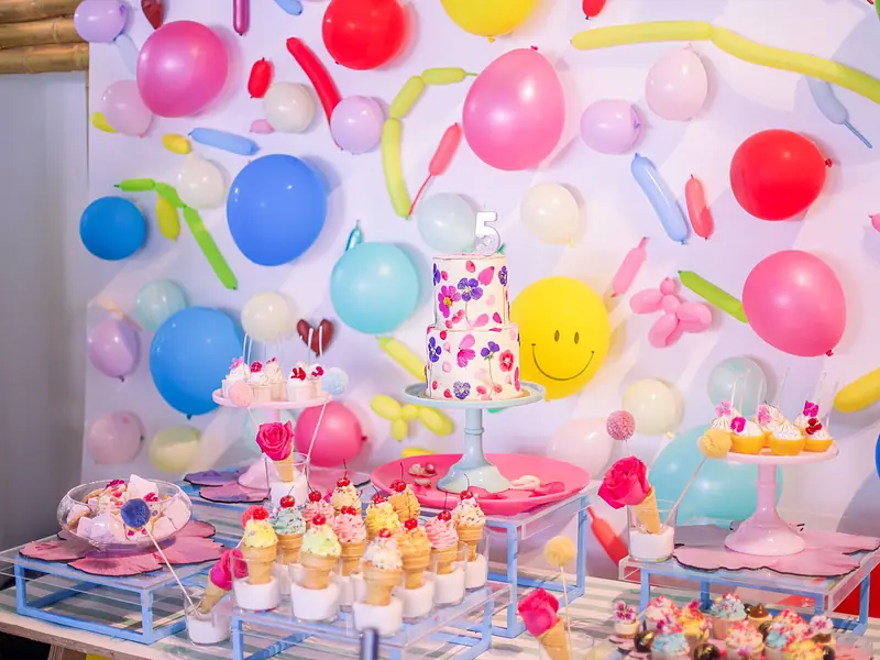 Mesa de dulces de cumpleaños infantil con fondo de globos de colores, cupcakes y postres