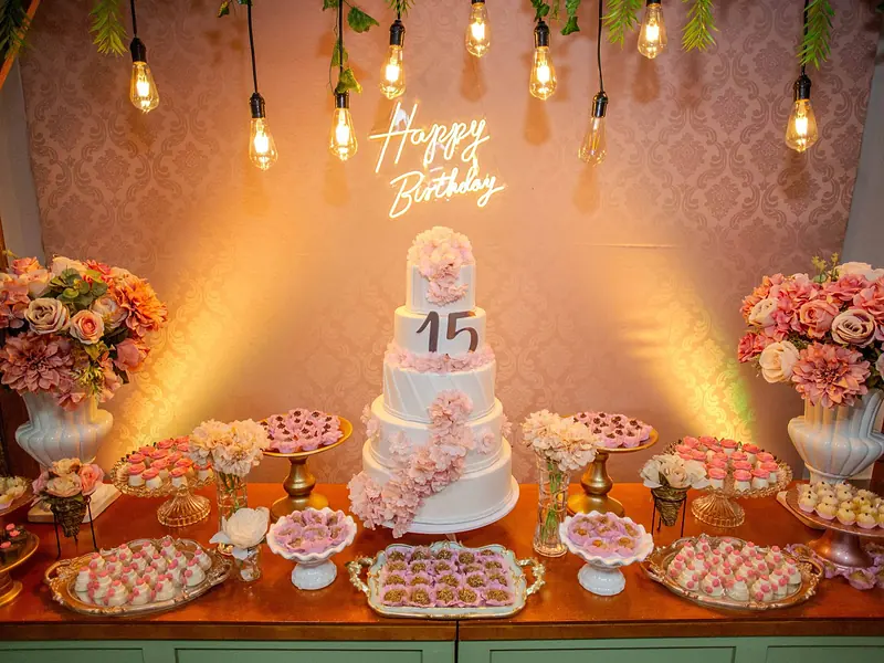 Mesa de dulces de XV años con pastel de pisos, letrero luminoso y postres en tonos rosa